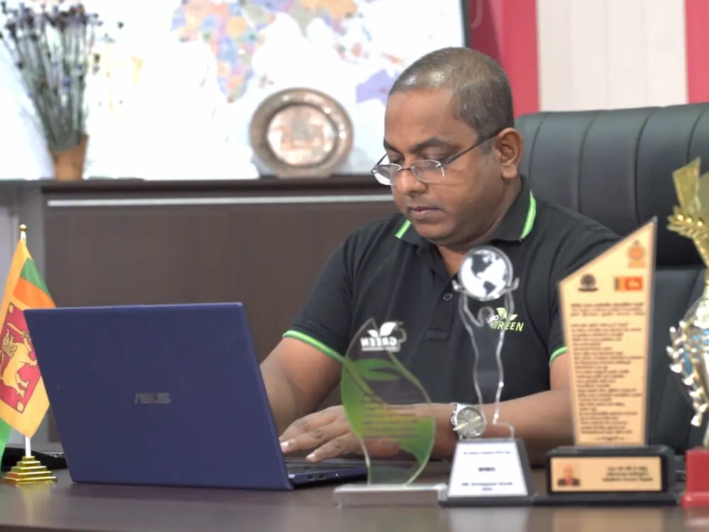 Mr. Chameel Samaranayake, Managing Director of Go Green Exports, at his desk with the company's export awards and the Sri Lankan flag